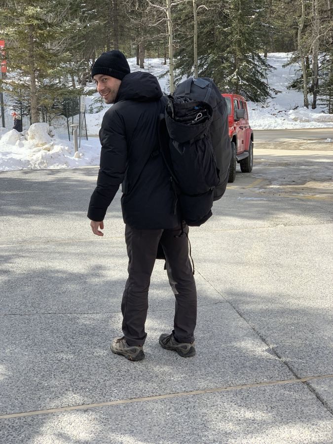 Manny smiling back over his shoulder, carrying a large backpack in a snowy mountain town